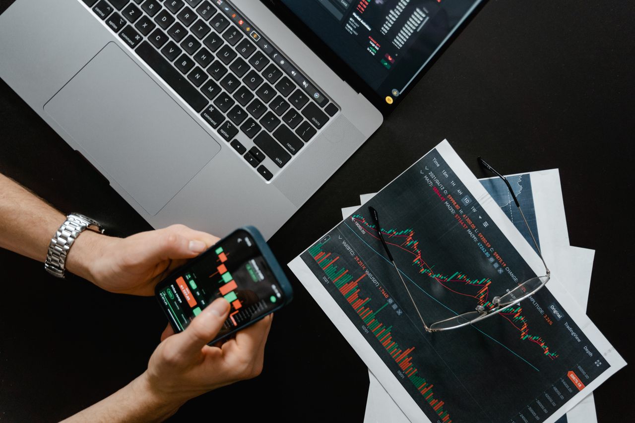 Services Hands using smartphone beside laptop with stock charts, showcasing digital trading.